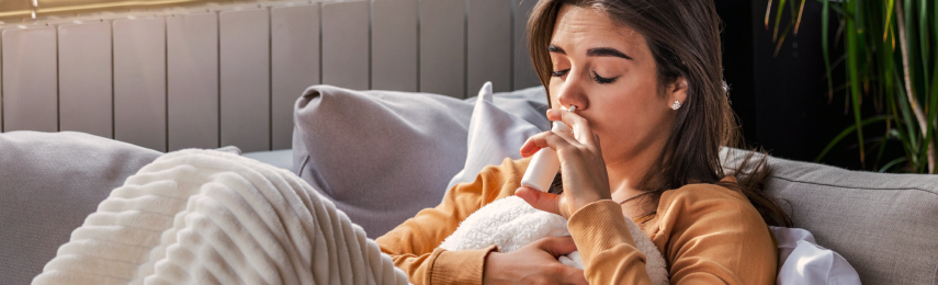 Giovane donna sul divano che usa lo spray nasale