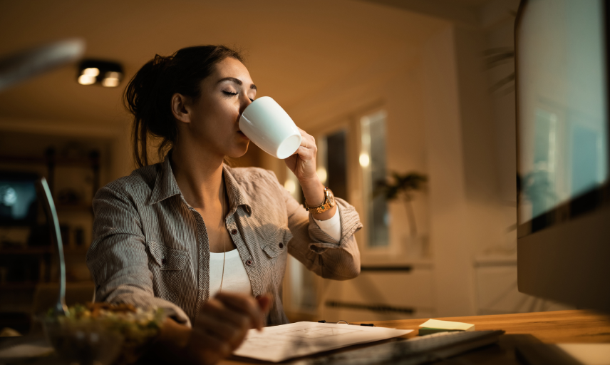 Giovane donna seduta alla scrivania che beve dalla tazza