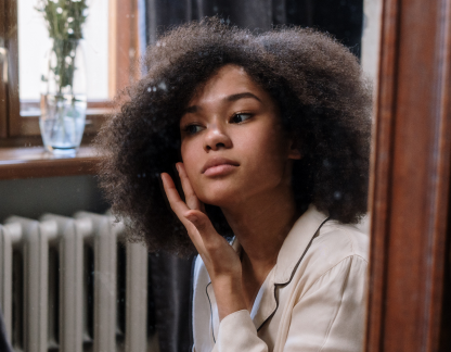 Ragazza si guarda allo specchio e spalma una crema sul viso