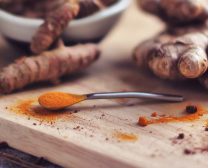 Close up di un cucchiaino di curcuma su uno sfondo di zenzero